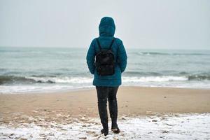 Girl in down jacket standing on seashore in winter photo