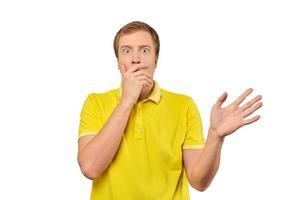 Frightened young man in yellow T-shirt holding hands over face, white background, afraid, negative photo