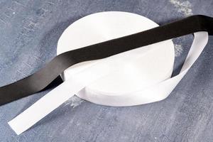 A closeup shot of a roll of white ribbon and a black ribbon strip on a blue table photo