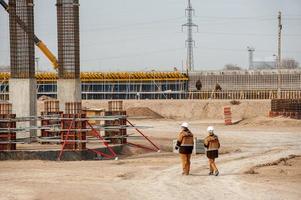 Two workers in special equipment and white helmets with a huge factory construction in the background photo