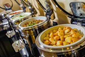 una mesa de buffet con recipientes llenos de patatas y platos de carne foto