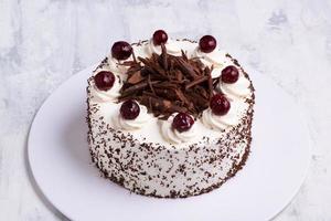 A closeup shot of white cream on Black Forest gateau cake with cherries on white marble surface photo