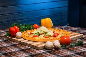 un primer plano de la mesa para el almuerzo, pizza, verduras, pimientos amarillos y rojos, champiñones en tablero de madera foto