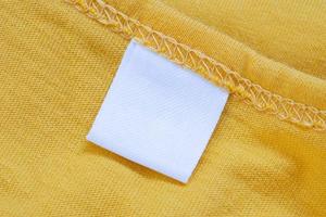 White blank clothing tag label on new yellow shirt background photo