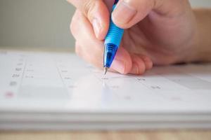 mano de mujer con bolígrafo escribiendo en la fecha del calendario concepto de reunión de cita de planificación empresarial foto