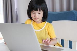 little asian girl student study online using laptop computer at home photo