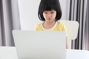 una pequeña estudiante asiática estudia en línea usando una computadora portátil en casa foto