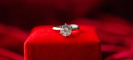 anillo de diamantes con caja de regalo de joyería sobre fondo de tela roja foto