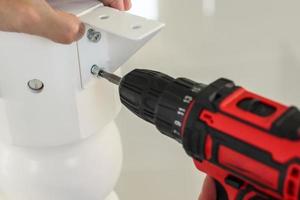 man assembling white table furniture at home using cordless screwdriver photo