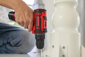 man assembling white table furniture at home using cordless screwdriver photo