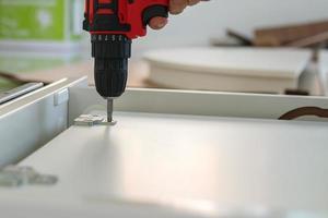 man assembling white table furniture at home using cordless screwdriver photo