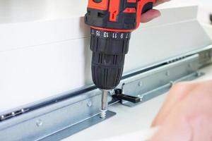 man assembling white table furniture at home using cordless screwdriver photo