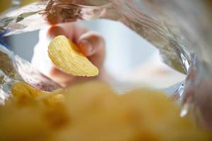 Hand picking potato chips inside snack bag photo