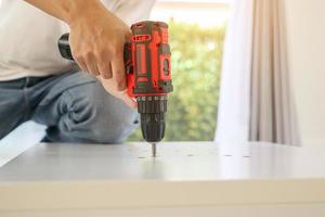 man assembling white table furniture at home using cordless screwdriver photo
