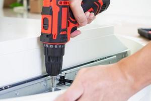 man assembling white table furniture at home using cordless screwdriver photo