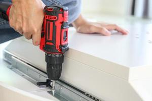 man assembling white table furniture at home using cordless screwdriver photo