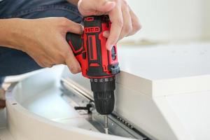 man assembling white table furniture at home using cordless screwdriver photo