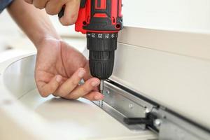 man assembling white table furniture at home using cordless screwdriver photo