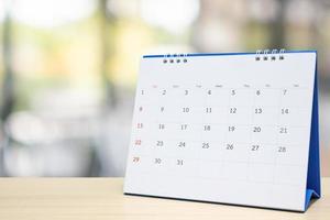 white paper desk calendar on wood table with blurred bokeh background appointment and business meeting concept photo