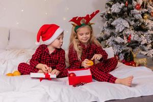 two happy children in pajamas for Christmas are sorting presents and playing with Christmas toys. High quality photo