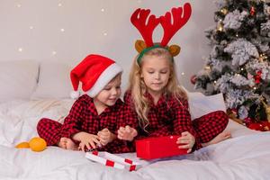 dos niños felices en pijama para navidad están clasificando regalos y jugando con juguetes navideños. foto de alta calidad