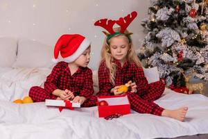 two happy children in pajamas for Christmas are sorting presents and playing with Christmas toys. High quality photo