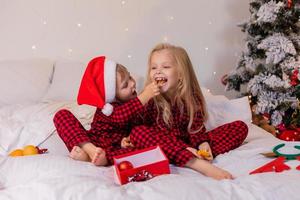 dos niños felices en pijama para navidad están clasificando regalos y jugando con juguetes navideños. foto de alta calidad