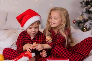 dos niños felices en pijama para navidad están clasificando regalos y jugando con juguetes navideños. foto de alta calidad