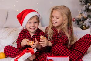 two happy children in pajamas for Christmas are sorting presents and playing with Christmas toys. High quality photo