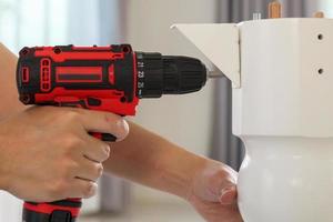 man assembling white table furniture at home using cordless screwdriver photo