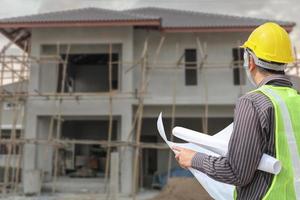 young professional engineer in protective helmet and blueprints paper at the house building construction site photo