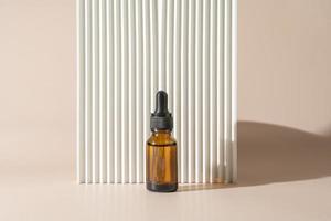 A face or hair serum or essential oil in a brown dropper bottle standing next to a white ceramic plate. Product marketing cosmetics mockup photo