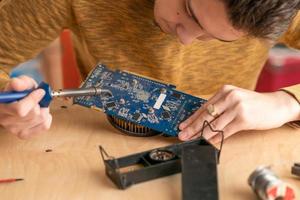 a young man solders a burnt-out microcircuit with a soldering iron photo
