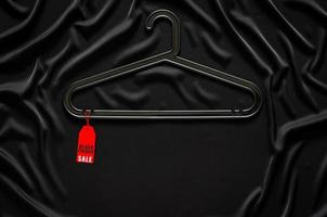 A black hanger with red price tag on black smooth and wavy cloth with space for text. Black Friday concept. photo