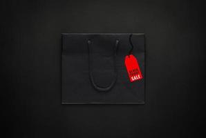 bolsa de papel de compras negra con etiqueta de precio roja sobre fondo negro para el concepto de venta de compras de viernes negro. foto