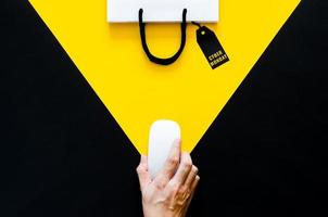 mano sosteniendo un mouse inalámbrico para comprar en línea con fondo amarillo y negro. concepto de lunes cibernético. foto