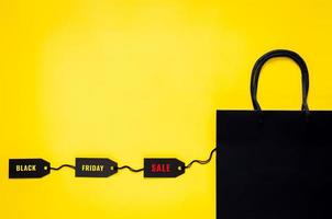 Black shopping paper bag with black price tags on yellow background for Black Friday shopping sale concept. photo