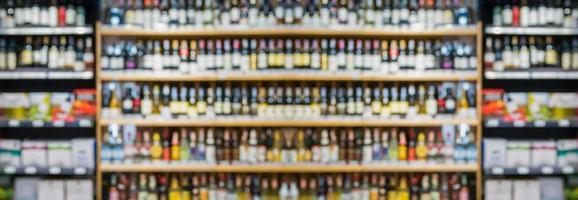 botellas de vino borrosas abstractas en estantes de alcohol de licor en el fondo de la tienda del supermercado foto