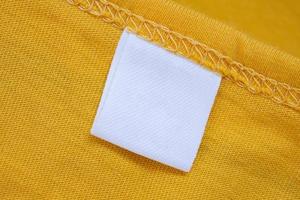 White blank clothing tag label on new yellow shirt background photo