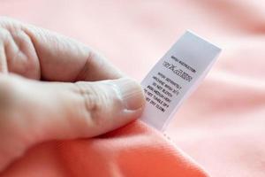 Hand hold and reading at white laundry care washing instructions clothes label on pink shirt photo