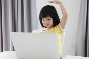 little asian girl student study online using laptop computer at home photo