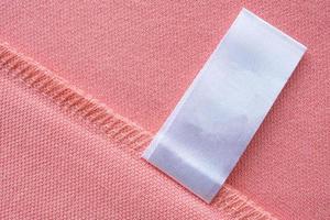 Blank white laundry care clothes label on pink fabric texture background photo