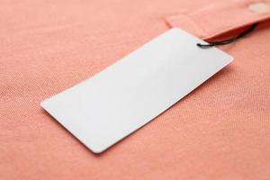 Blank white clothes tag label on pink fabric texture background photo