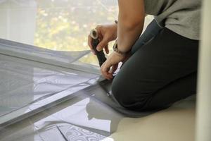 el hombre instala una pantalla de alambre de mosquitera en la ventana de la casa para protegerla contra insectos foto