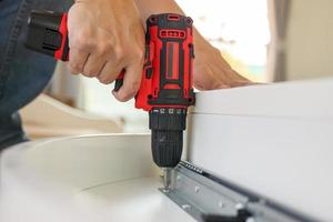man assembling white table furniture at home using cordless screwdriver photo