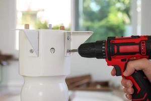 man assembling white table furniture at home using cordless screwdriver photo