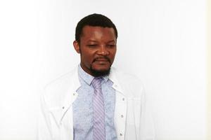 Serious black doctor man with small beard in white coat bright shirt looks down, white background photo