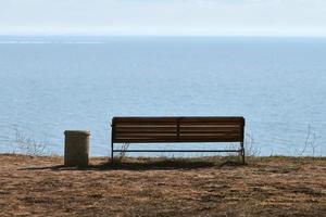 Empty bench with trashcan on cliff before sea background, peaceful quiet place for thinking alone photo