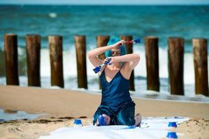 Artistic blue-haired woman performance artist smeared with blue gouache paints sitting on beach photo