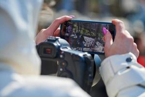 Woman videographer filming on DSLR camera and smartphone outdoor event, video photo blogging